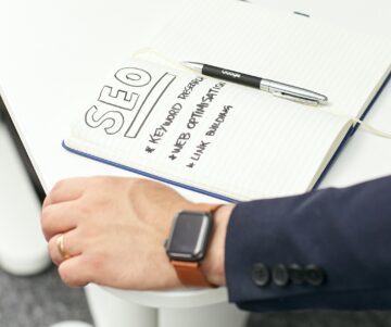 Bildet viser en skriveblokk, penn og en hånd på bordet.